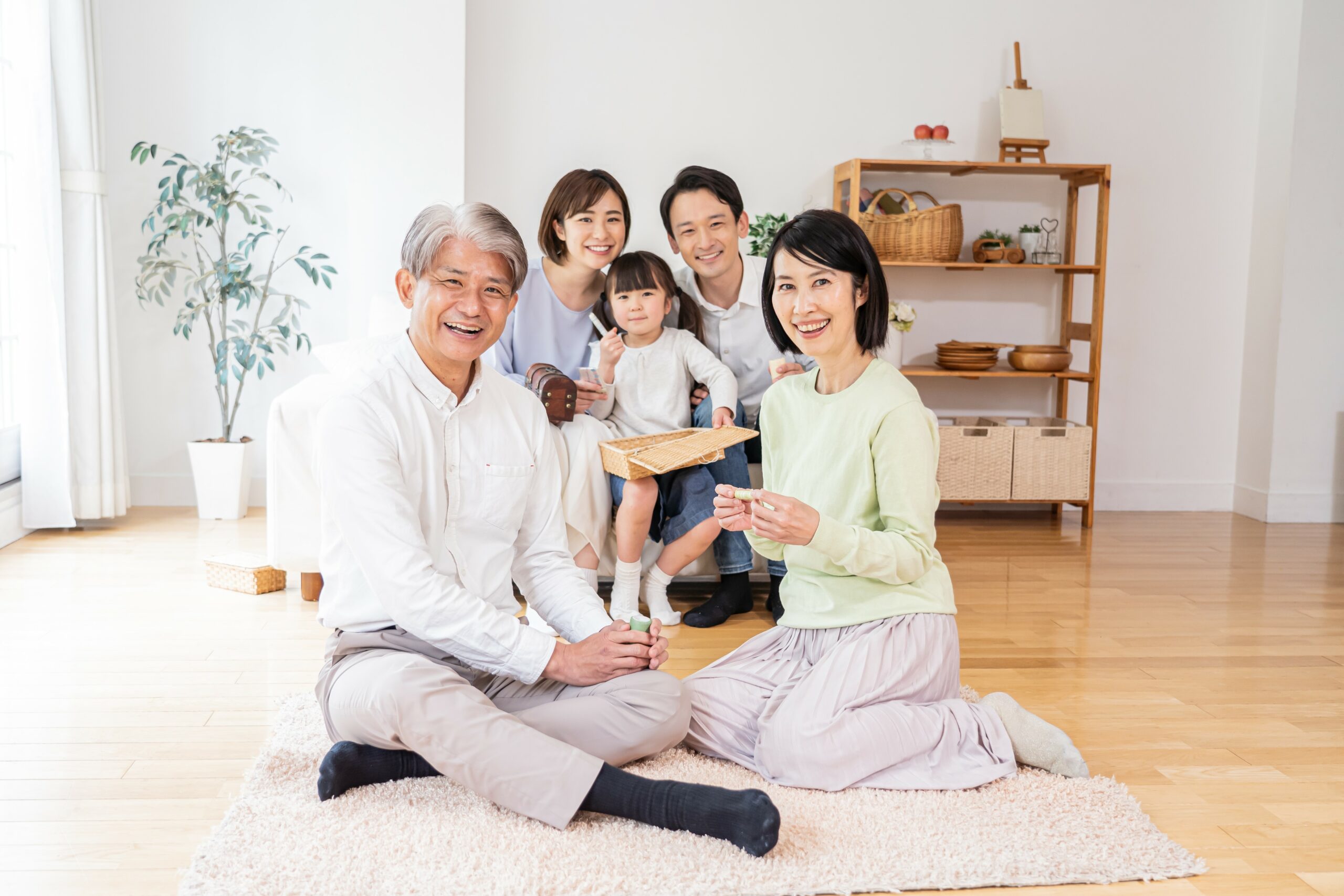 床に座り、笑顔でくつろぐ祖父母と両親と子どもの三世代家族