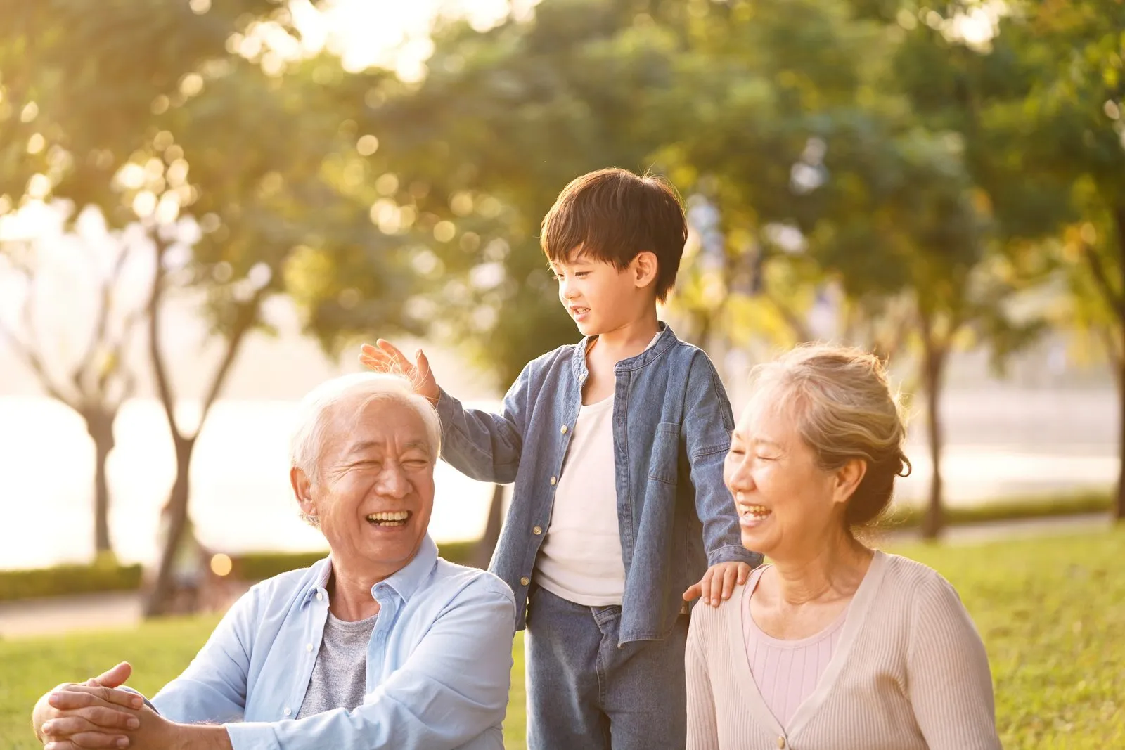 公園で笑い合う祖父母と、あいだに立つ孫の男の子