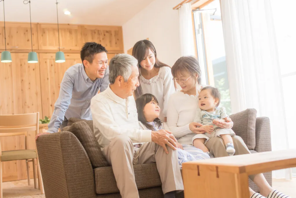 赤ちゃんを囲んで笑う祖父母・両親・子どもたちの三世代家族