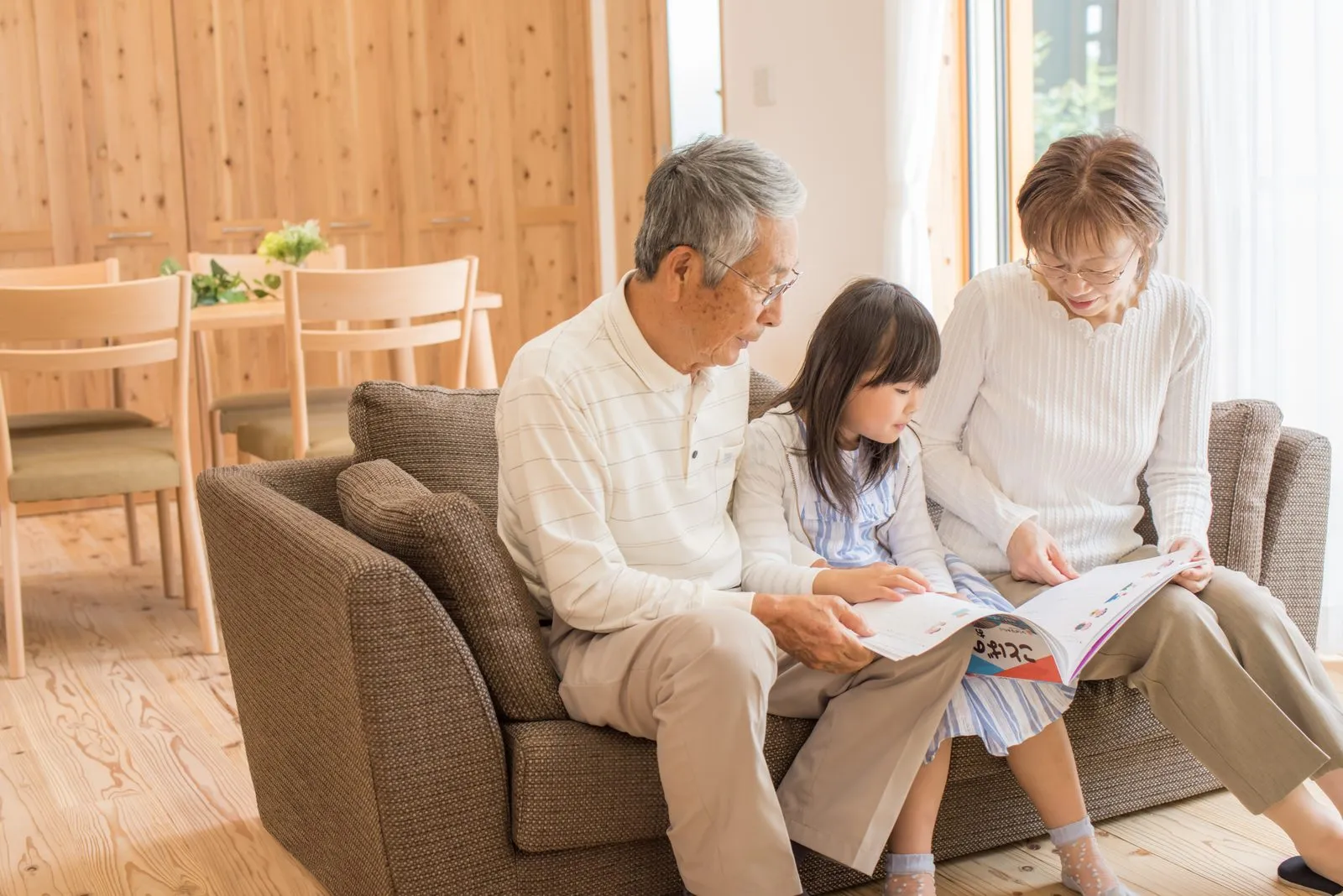ソファで孫と本を読む祖父母